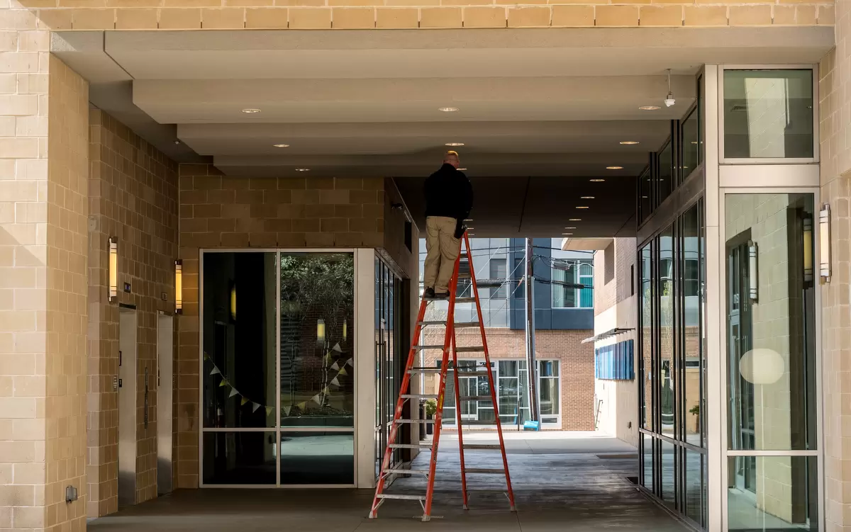 Handyman on a ladder fixing lights outside commercial property